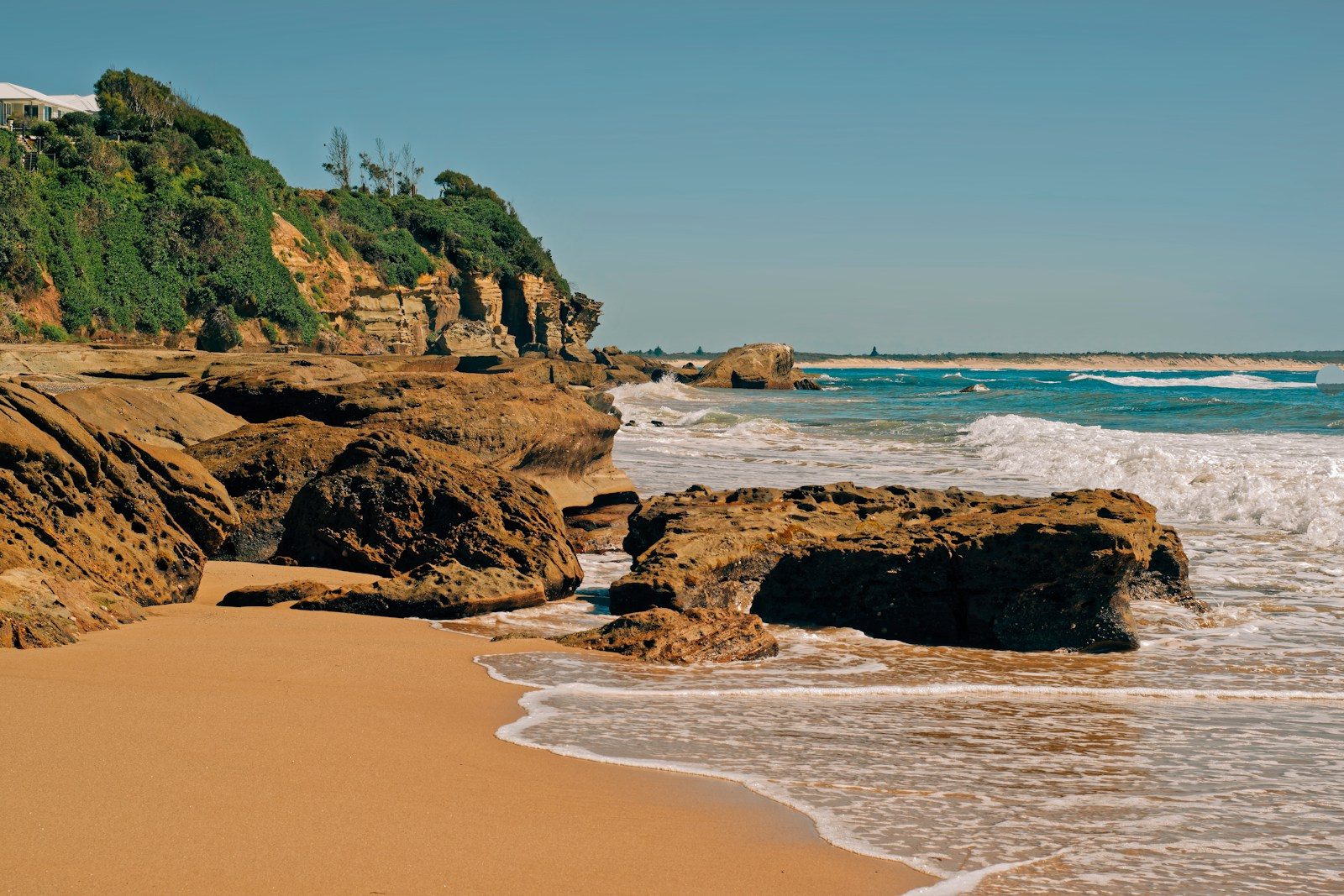 Rocky coastline with waves crashing on sandy beach.