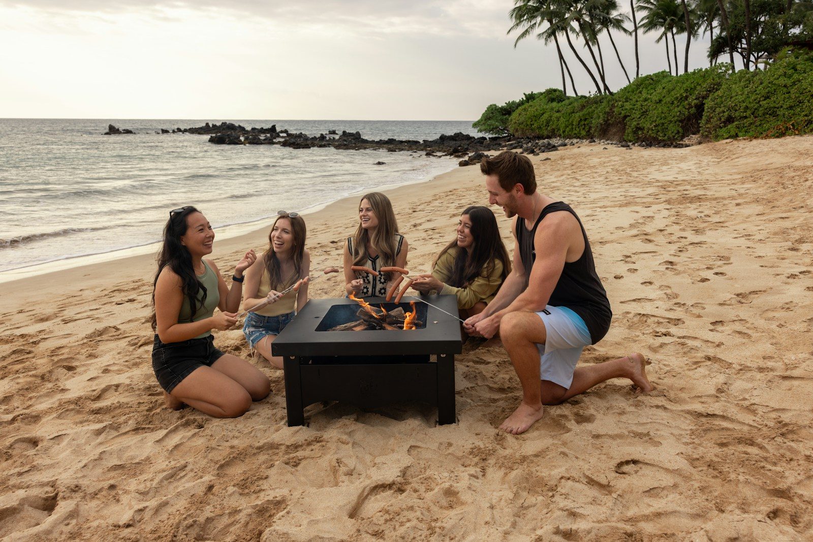 Friends gathered around a beach bonfire at sunset.