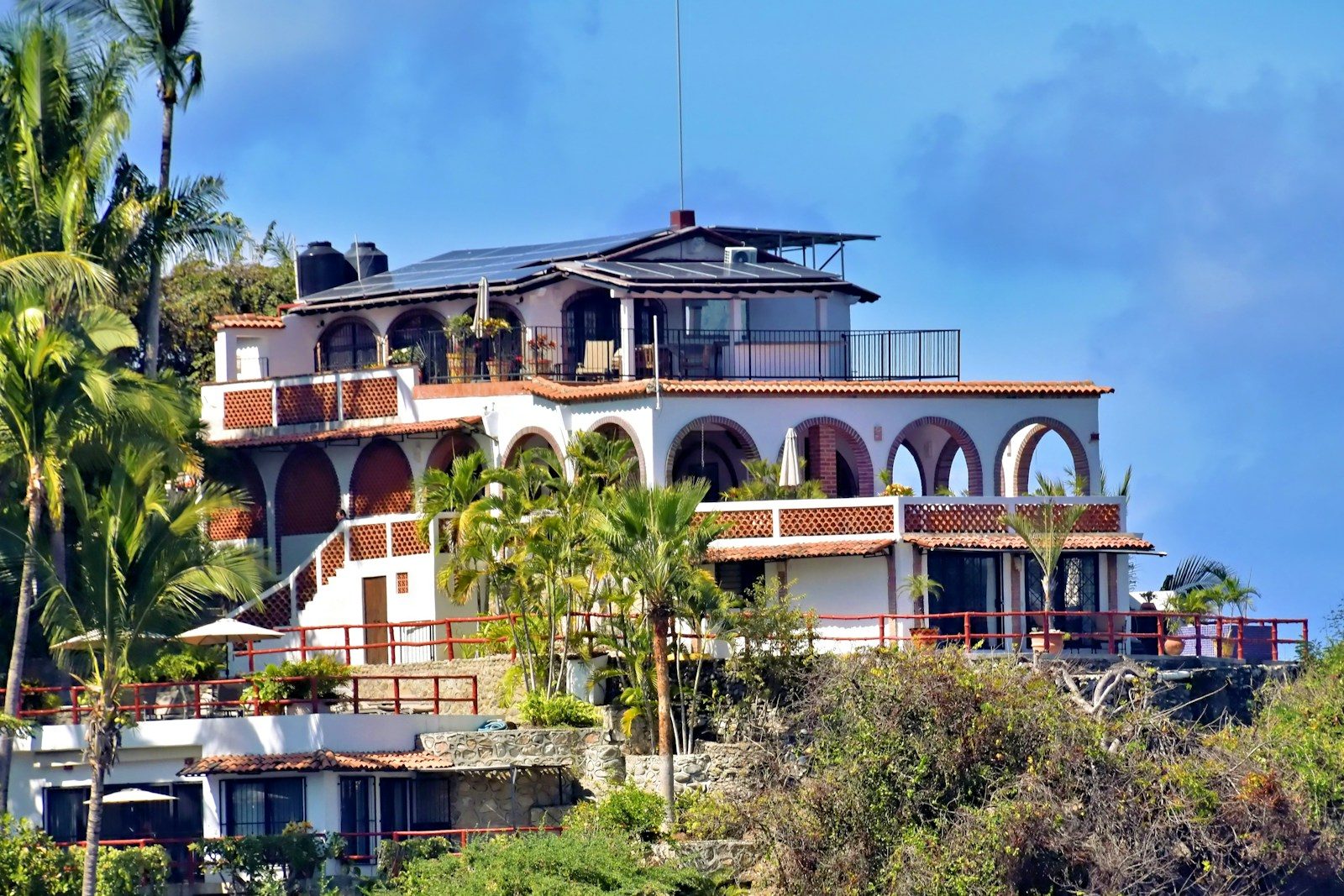 A large white villa on a hillside with palm trees.