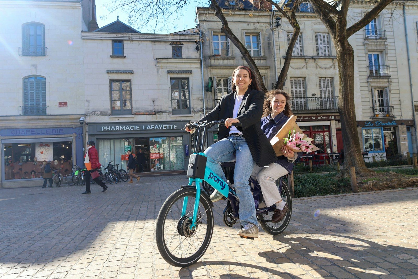 Two people ride a bicycle in a city square.